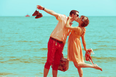 沙灘上散步的情侶。快樂的年輕人結婚時尚及膝