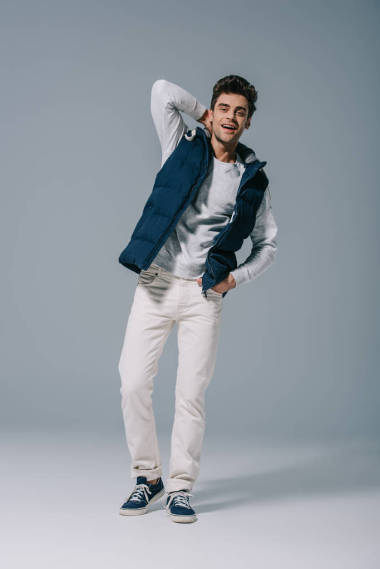 一位俊俏的笑脸男子穿着灰色的秋季背心摆姿势