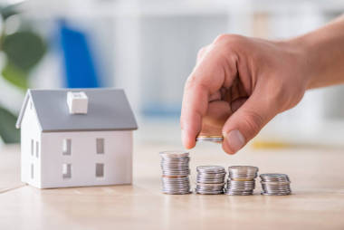 商人將硬幣堆在木制桌子上的房子模型附近的局部視圖