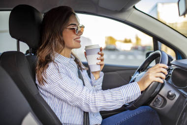 快樂的年輕女人喝咖啡去開車。 女人開車時喝了一杯咖啡。 年輕婦女開車時喝咖啡。 迷人的黑發(fā)女人開車
