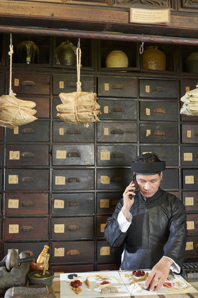 在药房工作并为顾客包装干根和浆果的亚洲传统医学从业人员 在药房工作并为顾客包装干根和浆果的亚洲传统医学从业人员