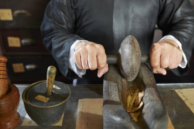 亞洲傳統(tǒng)醫(yī)學(xué)從業(yè)者的手在特殊的船用工具中研磨干草和樹(shù)根