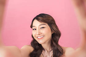 工作室肖像美丽的女人微笑与白色牙齿和自拍，拍摄自己粉红色背景