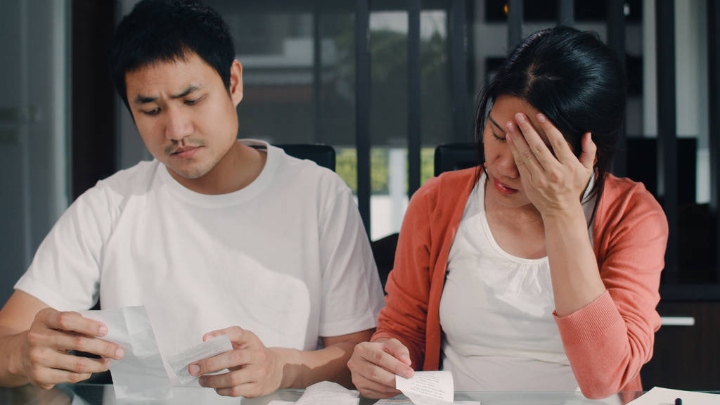 年轻的亚洲怀孕夫妇记录收入和开支在家里。妈妈担心，严重，压力，而记录预算，税收，财务文件工作在客厅在家里的概念