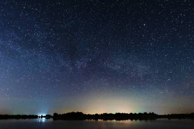 在河岸上的一个迷人的星夜，有一棵大树，天空中的一条银河，夏天有流星坠落
