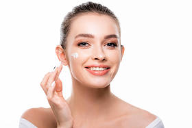 迷人的、面带微笑的女人在脸上涂化妆品，看着被白色隔离的相机