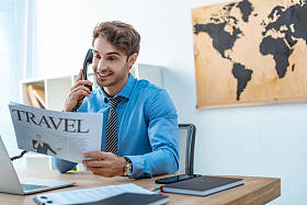 一边拿着旅游报纸一边微笑着与旅行社通电话