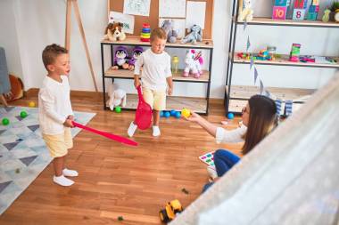 幼稚園里，漂亮的老師和幼兒用球拍在許多玩具周圍打網(wǎng)球