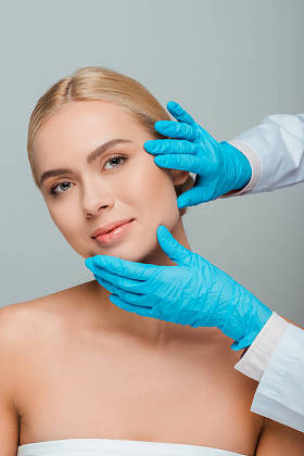 穿着蓝色乳胶手套的美容师触摸被灰色隔离的年轻女子的脸的剪影