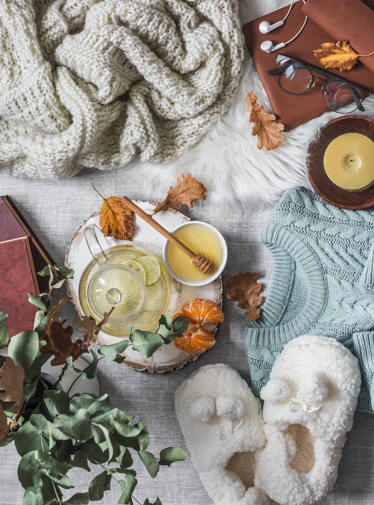 舒适舒适的家-柔软的拖鞋,针织毛衣,格子花,绿茶加蜂蜜,橘子,干叶,浅色背景的书,顶视图。 秋天和冬天有一种轻松的心情. 平躺 舒适舒适的家-柔软的拖鞋,针织毛衣,格子花,绿茶加蜂蜜,橘子,干叶,浅色背景的书,顶视图。 秋天和冬天有一种轻松的心情. 平躺