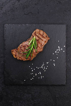 黑盘上有迷迭香枝条的牛排的顶部视图