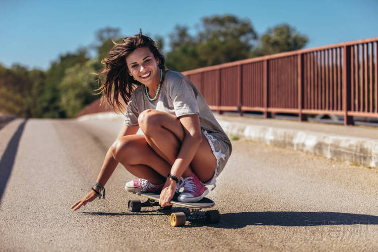 年輕的運動女人騎在滑板的道路上