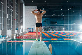 在游泳池附近触摸泳帽的英俊而强壮的游泳运动员 