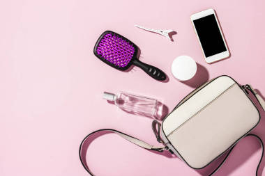 具有長柄和配件、電話、梳子、香水、粉色背景的乳霜的女裝十字形袋包。 班納 時尚與美的概念，現(xiàn)代的，時尚的。 平躺在地上，俯瞰四周