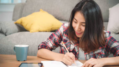 亞裔女學(xué)生在家做作業(yè)，女同學(xué)用平板電腦在客廳的房間里找。生活方式 婦女放松在家里的概念