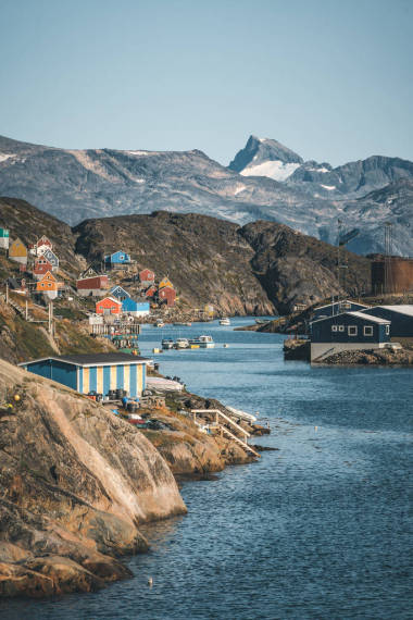 西格陵兰Kangaamiut渔镇的山坡上点缀着五彩斑斓的房屋。 格陵兰坎吉亚冰川的冰山带着蓝天和蓝云在游泳。 全球变暖的标志