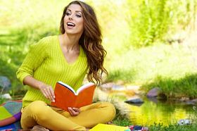 年轻漂亮的女人在绿色的原野上奠定了和看书