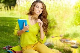 年轻漂亮的女人在绿色的原野上奠定了和看书