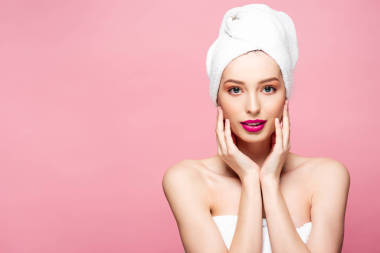 美丽的年轻女子穿着白色的毛巾触摸脸上孤立的粉红色