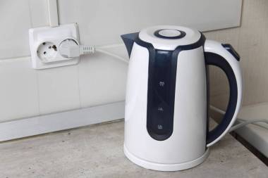 白色電水壺矗立在插在電源插座上的灰色桌子上