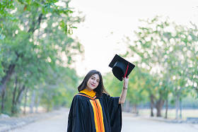 一位穿着学术礼服头戴研究生帽的年轻快乐的女毕业生在大学校园里开始庆祝她的大学学位