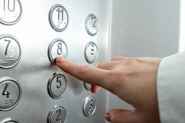 女性的手，手指按下電梯按鈕。晉升到事業(yè)的階梯上