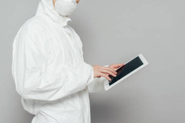 身著危險物品套裝、戴著口罩、手持灰色背景空白屏幕數(shù)碼平板電腦的流行病學家的剪影