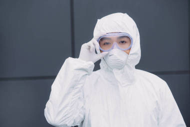 亞洲流行病學(xué)家穿著防護(hù)服戴著口罩站在外面觸摸護(hù)目鏡看著攝像機(jī)