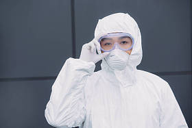 亚洲流行病学家穿着防护服戴着口罩站在外面触摸护目镜看着摄像机