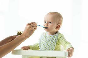 妈妈用蔬菜罐喂婴儿营养用勺子喂婴儿把喂养椅隔离在白色上