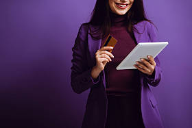 带着紫色背景的数码平板电脑和信用卡微笑的女人的剪影