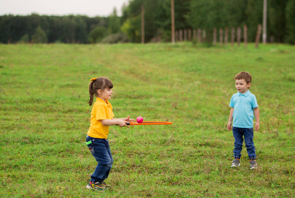孩子们- -一个穿着蓝色T恤的男孩和一个穿着黄色球衣、带着球拍和球拍的女孩在一起打网球