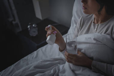 睡眠障礙婦女在臥室拿著一杯水和裝有安眠藥的瓶子的剪影 