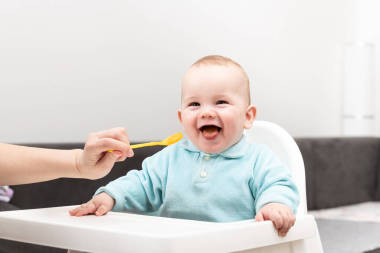 快樂(lè)的媽媽、保姆或姐姐在家里給小寶寶喂食一勺食物
