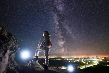 可以看到太空旅行者站在巖石山上，欣賞著星空、銀河和夜城的美景。身穿白色宇航服的飛行任務(wù)專業(yè)宇航員。空間旅行的概念