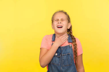 流感癥狀，頸部疼痛。穿著粗斜紋棉布工作服的生病小女孩的畫像，患有喉炎或扁桃體炎、甲狀腺疾病、醫(yī)學(xué)問題。在黃色背景下隔離的室內(nèi)拍攝