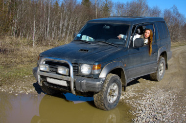 年輕女子越野汽車前水障礙的土路上的方向舵背后