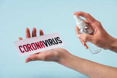 一名婦女手持裝有洗手液的噴霧瓶靠近藍色隔離的冠狀病毒字母卡片