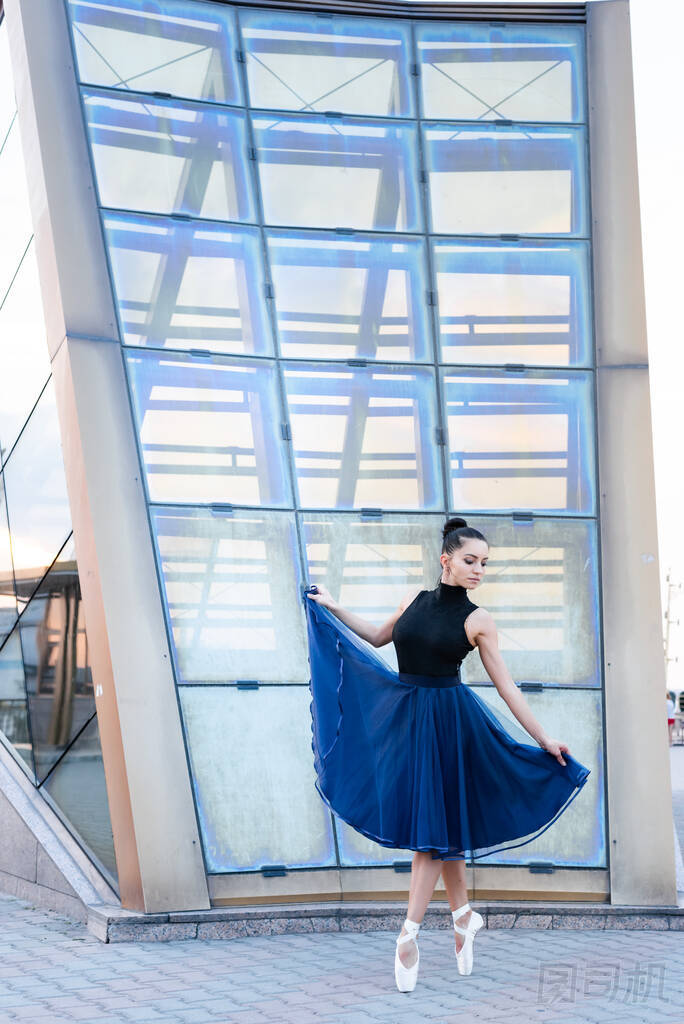 漂亮的芭蕾舞演員穿著藍色的衣服,身姿端莊,跳舞,練習伸展動作和經(jīng)典的練習.芭蕾舞女穿著尖皮鞋在城市里跳舞