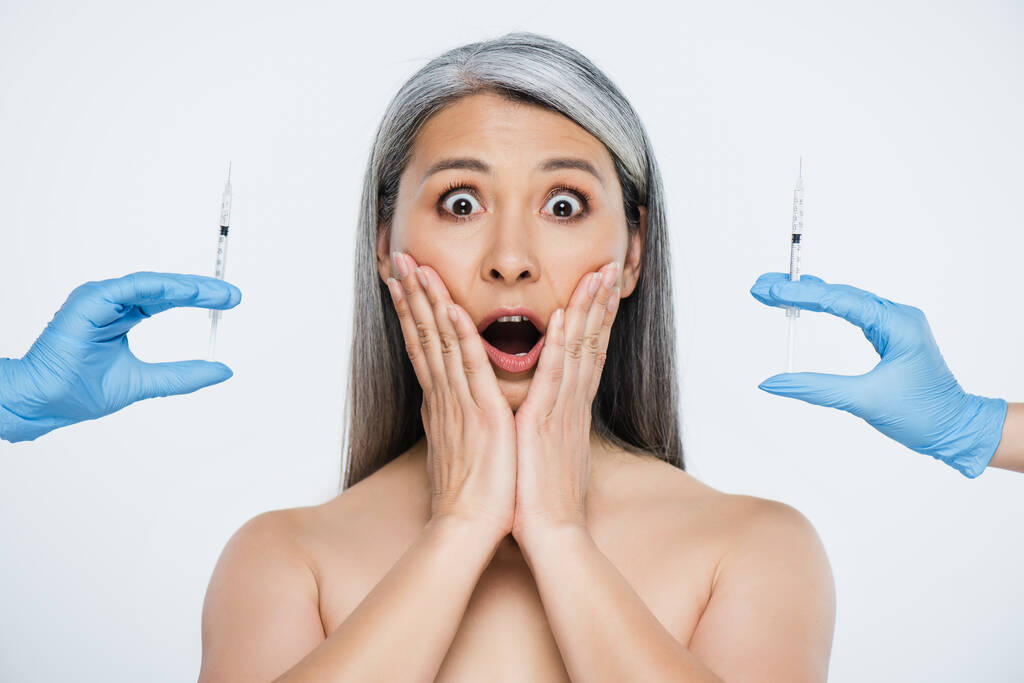 穿着乳胶手套的亚洲裸体女性和医生们震惊不已，他们拿着注射器，注射器上的美感是用灰色隔开的
