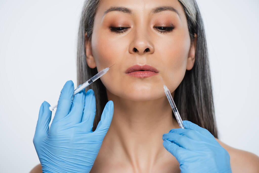 漂亮的裸体亚洲女人和医生戴着乳胶手套，拿着注射器，注射器上有灰色的漂亮注射