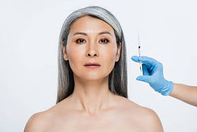 漂亮的裸体亚洲女人和医生，戴着乳胶手套，拿着注射器，用灰色隔离的漂亮注射器