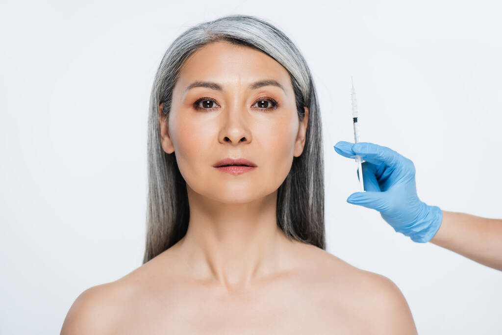 漂亮的裸体亚洲女人和医生，戴着乳胶手套，拿着注射器，用灰色隔离的漂亮注射器