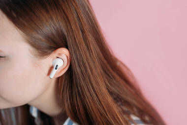 女孩在無(wú)線(xiàn)耳機(jī)上轉(zhuǎn)換音樂(lè)。空氣泵專(zhuān)業(yè)。與無(wú)線(xiàn)收費(fèi)案件。新的氣孔親粉紅背景。Airpodspro 。女耳機(jī)。復(fù)制空間