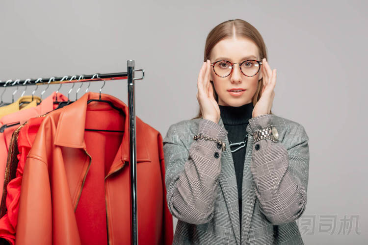 年輕的造型師在灰色的時髦衣服旁邊觸摸眼鏡 