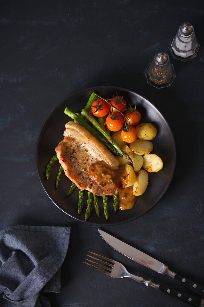 烤猪排,蔬菜放在黑盘上.头顶垂直图像 烤猪排,蔬菜放在黑盘上.头顶垂直图像