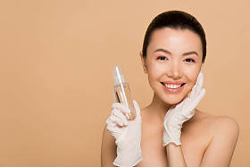 穿着乳胶手套的漂亮而快乐的裸体亚洲女孩，手里拿着用米黄色隔热的防腐