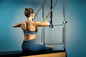 年轻的女孩在普拉提改革者的床上练习，在大厅的灰色墙壁的后面。健身伸展的概念。健康的身体，瑜伽，普拉提，复制空间