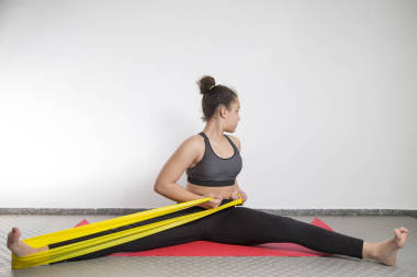 女孩在家里用橡皮筋訓(xùn)練。長腿和灰色上衣。健康概念