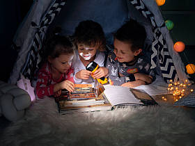 The three children sat in their tent at night by the light of their torches reading an interesting book about treasure Island adventures. Pirate games. Learn to read in a fun way